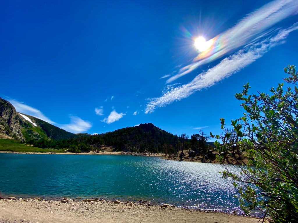 Mountain lake with sun shining down, creating a rainbow in the cloud